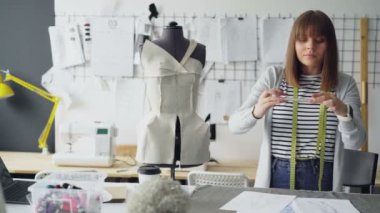 Genç iddialı terzi giysi çizimler onun modern ışık studio smartphone kullanarak tablo yalan fotoğrafını çekmek. Kendinden emin ve konsantre bir kadındır.