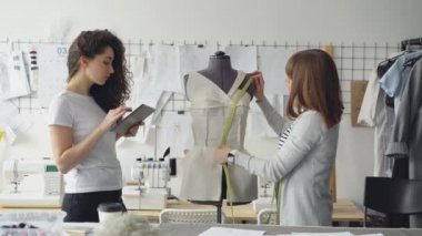 Onun iş arkadaşı ölçüm verileri yazmak için tablet ile çalışırken profesyonel terzi şablonlarını ölçü-bant ile manken üzerinde ölçmek.