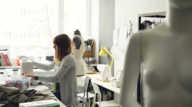Yan görünüm ışıkta dikiş makinesi ile çalışan genç kadın terzi dükkanı yapılandırılabilir. Kadın donatım ayarlama ve dikkatle Tekstil dikiş.