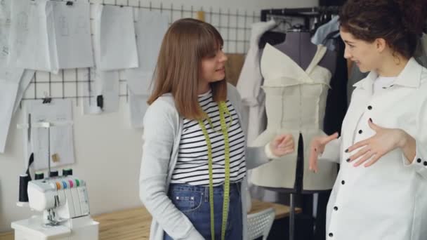 Pretty customer is trying on tailored shirt and sharing her opinion while clothing designer is measuring and checking garment and taking to client in light studio. — Stock Video