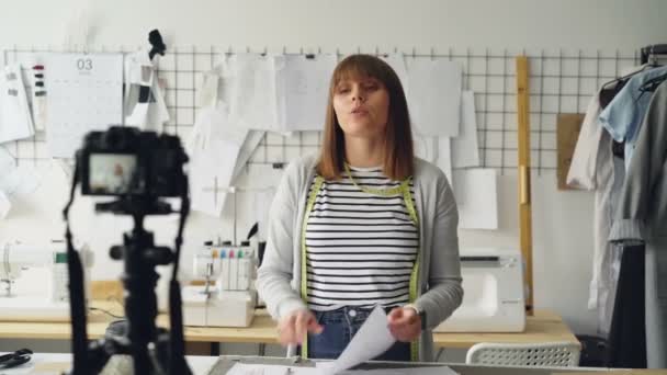 Die junge Bloggerin Schneiderin dreht für Instagram ein Video über die Gestaltung von Damenbekleidung. Sie grüßt Follower, zeigt Sketche, spricht emotional und gestikuliert. — Stockvideo