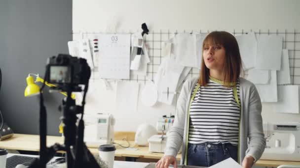 Blogueira criativa está gravando vídeo sobre sua nova coleção de roupas usando a câmera. Ela está mostrando esboço e falando sobre isso emocionalmente para videoblog . — Vídeo de Stock