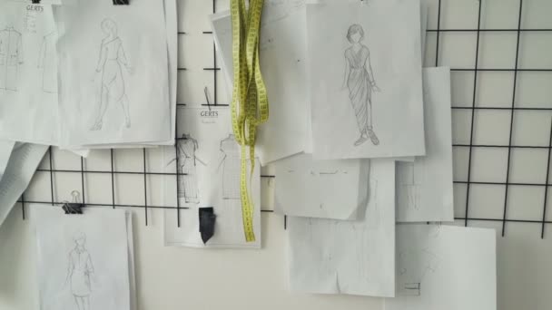 Panorámica de bocetos en blanco y negro, dibujos y notas con medidas de prendas de mujer en la pared en el estudio de diseño de ropa. Creación de un nuevo concepto de colección . — Vídeos de Stock