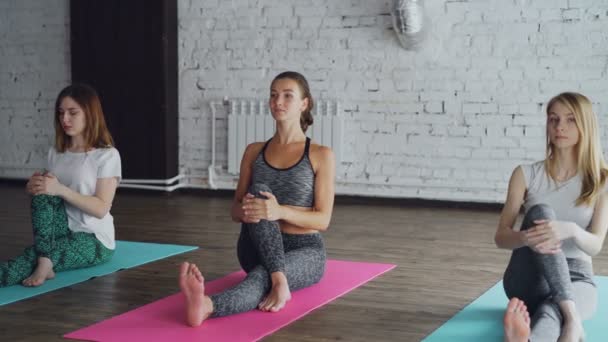 Los estudiantes de yoga están sentados en esteras y haciendo una pose de yoga giratoria luego estirando la pierna, perdiendo el equilibrio y riéndose juntos. Diversión en yoga concepto de estudio . — Vídeos de Stock