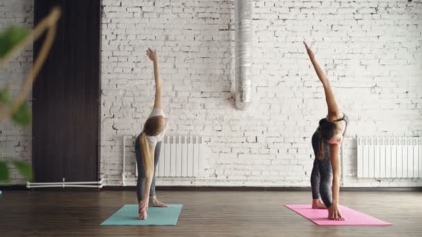 Опытный учитель йоги демонстрирует расширенную треугольную позу для юной блондинки и корректирует положение своего тела во время индивидуальной практики. . — стоковое видео