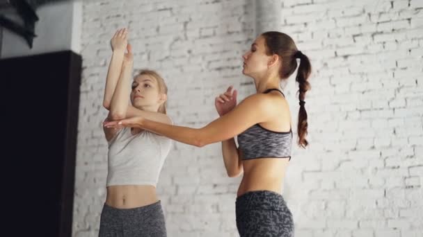 Профессиональный инструктор йоги обучает нового студента делать повороты рук, имея индивидуальную практику в велнесс-студии. Девушки смеются во время упражнений, расслабляющая атмосфера . — стоковое видео