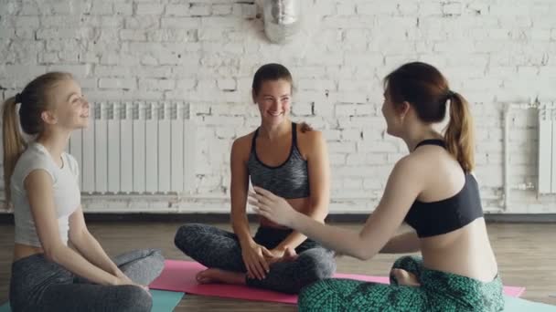 Jonge vrolijke vrouwen zijn gezelligheid na yoga praktijk zittend op matten in cirkel in lichte studio. Ze zijn emotioneel praten, lachen, gebaren. Wellness leuk concept. — Stockvideo