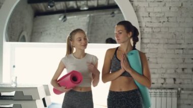 Genç kadın yoga öğrencilerin pratik beyaz duvarları ve çeşitli spor malzemeleri ile modern studio ile yürürken sohbet. Sağlıklı yaşam mutluluk kavramı.