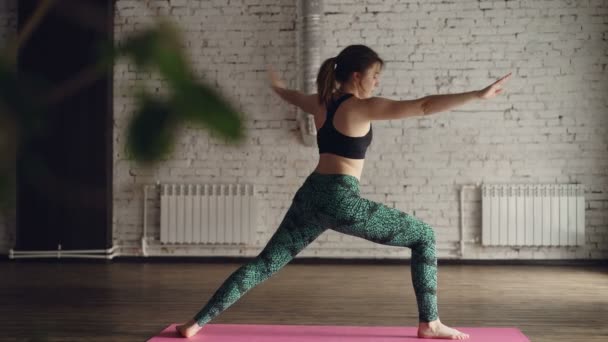 Giovane donna in abbigliamento sportivo alla moda sta praticando yoga durante la pratica individuale nel moderno centro benessere. Sta facendo una sequenza di asana popolari . — Video Stock
