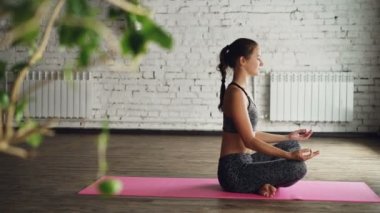 Rahatlatıcı ve parlak mat lotus pozisyonda otururken nefes yoga öğrenci yan görünüm. Çekici kadın Sağlık Merkezi uzun uygulama sonra dinlenme geçiriyor.