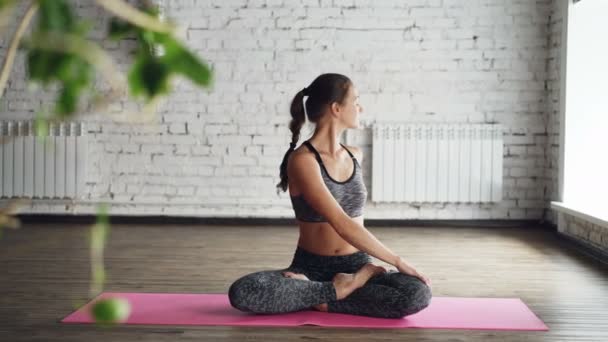 Instructora de yoga bastante femenina está demostrando giros corporales en posición de loto, estirándose y haciendo namaste luego relajándose con las manos en las rodillas y respirando . — Vídeos de Stock