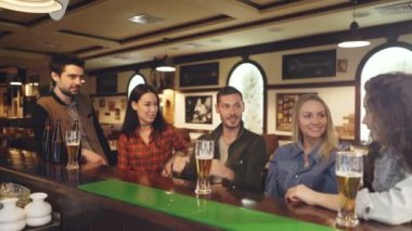Arkadaş grubu oturuyor bar sayacı ve konuşuyor. Bira gözlük ve şişeler, tablolar görülebilir. Dost gayri resmi bir atmosfere.