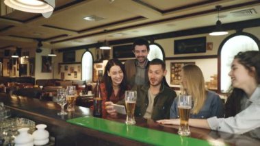 Arkadaşlar smartphone izlerken, söz, otururken gülüyor sayaç barda. Yakışıklı genç insanlar heyecan ve zevk gece.