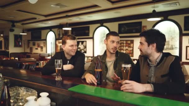 Colegas do sexo masculino estão conversando no bar local. Colaboradores que se reúnem fora do local de trabalho e se comunicam informalmente. Bom interior pub no fundo . — Vídeo de Stock