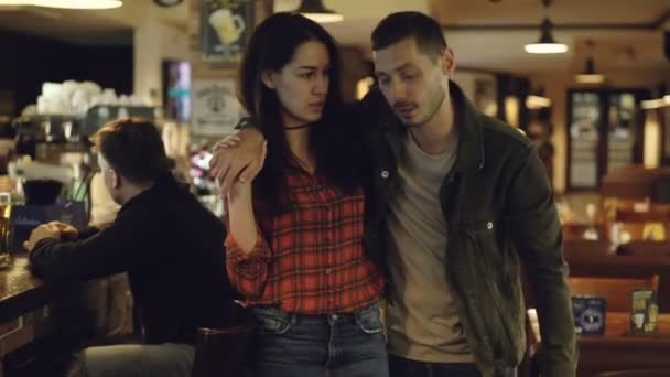 Young brunette is leading her drunk husband out of bar. Unshaven handsome young man is talking to his upset wife trying to explain himself. Alcoholism ruining family concept. — Stock Video