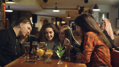 Kafede masada otururken genç kadın komik bir şey onun smartphone ekranında arkadaşlarına gösteriyor. Onu arkadaşları gülüyor ve bu konuda konuşmak.