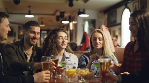 Los estudiantes están celebrando el final de la sesión académica en el moderno pub. Están brindando, tintineando vasos y bebiendo bebidas alcohólicas. Los jóvenes se están divirtiendo . — Vídeo de stock