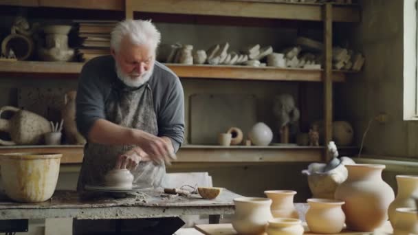 Experienced ceramist is creating utensils from clay on throwign wheel in workshop. Producing eathenware, handmade utensils and professional pottery concept. — Stock Video