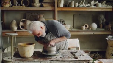 Yetenekli yaşlı potter işyerinde tekerlek dönme üzerinde seramik tencere üretiyor. Oluşturma işlemi, geleneksel seramik ve ilginç hobi kavramı.