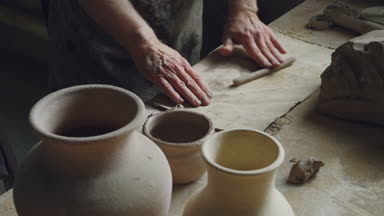 Üst düzey erkek ustası, kirli eller kil küçük parça çalışma tablosu üzerinde haddeleme. El yapımı seramik kaplar ve kavanozlar, potters araçları görülebilir.