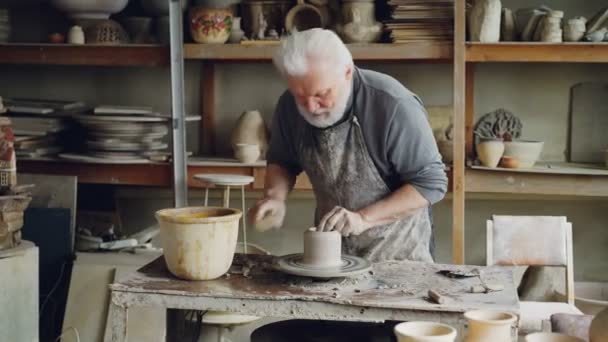 Senior férfi szakmai potter, hogy tál agyagból a fazekasok rokka, szélesítése és simító nedves clayware. Más kézzel készített kerámia figurák háttérben. — Stock videók