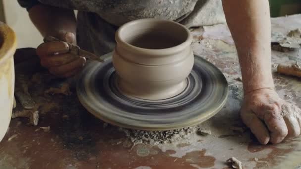 Close-up shot of male hands decorating ceramic pot with knife on spinning potters throwing wheel, making ornament. Pottery, hobby and handicraft concept. — Stock Video