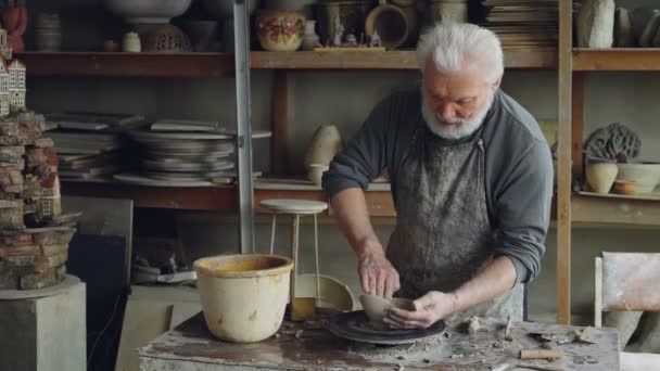 Der kreative männliche Töpfer formt während seiner Arbeit in einer kleinen Werkstatt eine unsymmetrische breite Schale auf einer Wurfscheibe. Kreativität, Töpfern und ungewöhnliches Hobby-Konzept. — Stockvideo