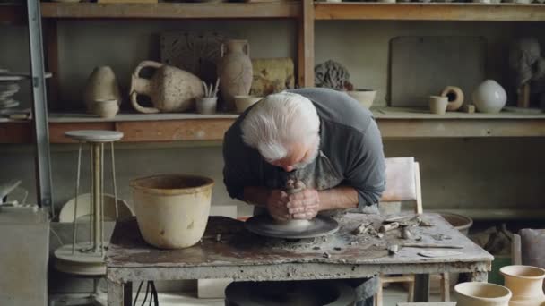 Potier sénior créatif mouille les mains dans un bol avec de l'eau et toucher un morceau d'argile sur la roue tournante. L'homme barbu est concentré sur le travail . — Video