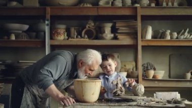 Sevimli küçük çocuk dedeleri atölyesinde seramik oyuncak yapma kil ile oynuyor. Gri saçlı sakallı adam ona aşk ve gurur ve konuşmak ile bakıyor.