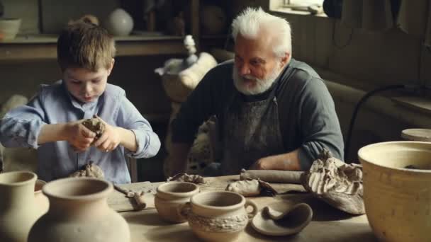 Kind is het leren om te werken met klei en plezier kneden het tijdens uw verblijf bij zijn grootvader in zijn atelier aardewerk. Familie traditie en keramiek concept. — Stockvideo