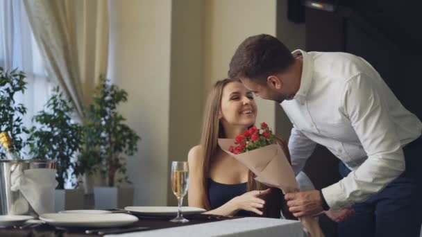 Gelukkig vriendin wordt steeds bloemen en presenteren van haar vriendje na een wachttijd van hem alleen in het restaurant. Romantische relatie, geschenken en fine dining concept. — Stockvideo