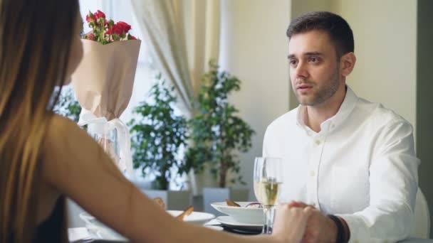 Un chico guapo bien vestido le está haciendo una propuesta a una jovencita mientras cena en un restaurante. Él está hablando y luego le da su anillo de compromiso en el joyero . — Vídeo de stock