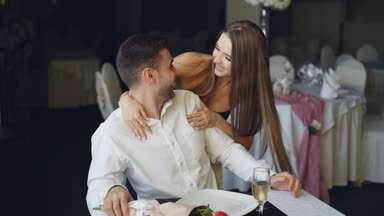 Genç ve güzel kadın sevgilisi sarılma ve onu, o zaman çiçek alarak ve onun önünde masada oturan öperken elleri, gözleri kapanış restoranda tebrik.