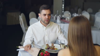Genç çift restoranında yemek, bağırarak ve mimik kavga. Şampanya bardağı ve gıda ile plakalar kıvılcım gül buketi görünür.