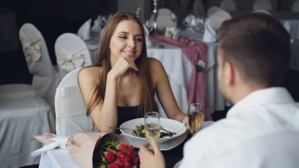 Chica alegre en hermoso vestido está hablando con su novio y riendo mientras cenan juntos en el restaurante. Conversación, comer fuera y gente feliz concepto . — Vídeos de Stock