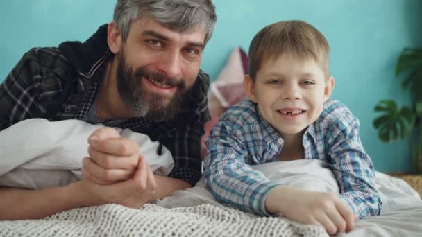 Nahaufnahme Porträt von zwei Menschen erwachsenen Vater und niedlichen kleinen Sohn zu Hause auf dem Bett liegend und lächelnd. Vaterliebe, Elternschaft und glückliches Familienkonzept.