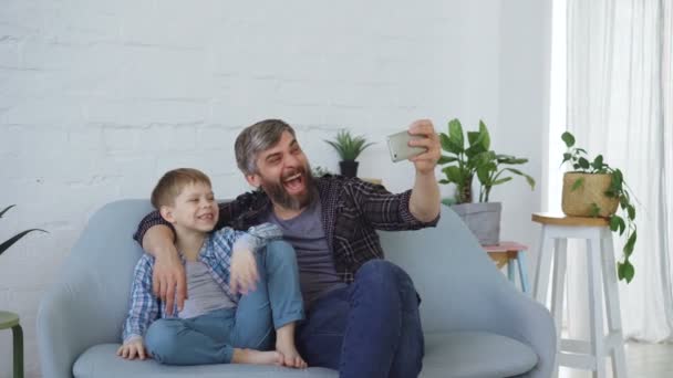 Komik adam sevgi dolu baba selfie gülüyor ve el hareketi, kamera için poz neşeli oğlu ile alıyor. Kendi portresi ve mutlu aile kavramı. — Stok video