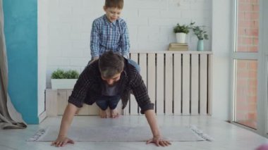 Güçlü aktif adam, gülen küçük oğlu sırtında otururken şınav çekiyor. Spor, aileyle vakit geçirmek, mutlu çocukluk kavramı..