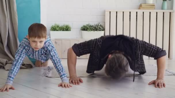 Active handsome father and his joyful son are exercising doing press-up together at home on wooden floor. Happy family, sport and sporty lifestyle concept. — Stock Video