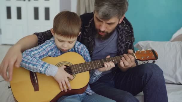 Koncentrerade barn är spela gitarr med hans far erfaren gitarrist, justera musikinstrument och njuter lyckliga stunder. Musik och familjen koncept. — Stockvideo