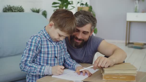 Bedårande barn junior school student gör läxor skriver i motion bok med hans far. Utbildning, barn utveckling, föräldraskap och barndom koncept. — Stockvideo