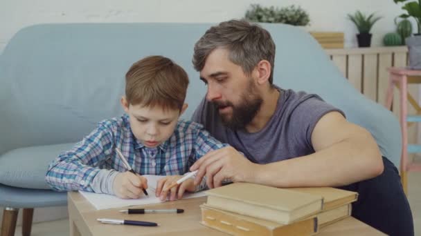 Barn lärande, skriva ord i Skrivbok och hans far undervisar honom sitta nära bordet och förklara reglerna till sin son. Utbildning, barndom och faderskap koncept. — Stockvideo