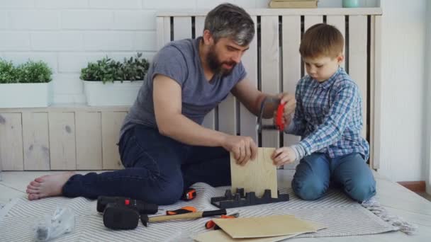 Pai barbudo e pequeno filho bonito fazendo casa de pássaros de lençóis de madeira em casa. Conceito de infância e paternidade fazendo high-five para celebrar o trabalho bem sucedido . — Vídeo de Stock