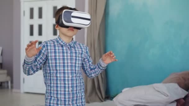 Adorable little boy is trying virtual reality glasses and gesturing while standing in his apartment. Modern technology, entertainment and people concept. — Stock Video