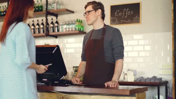 Jolie jeune femme achète un café à emporter dans un café-restaurant et paie avec un smartphone en effectuant un paiement sans contact. Technologie moderne et concept bancaire . — Video