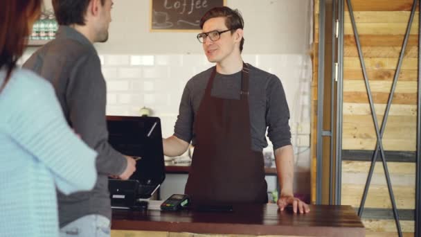 Joyeux caissier amical prend les commandes de clients debout en ligne, accepter le paiement sans contact avec téléphone intelligent et la vente de café à emporter . — Video