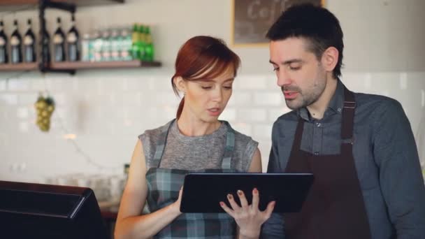 有吸引力的年轻人咖啡屋老板们在柜台工作时用平板电脑说话。伙伴关系、成功青年与现代技术理念. — 图库视频影像