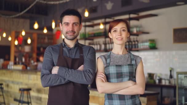 Retrato de dos camareros alegres parados dentro de una acogedora cafetería, sonriendo y mirando a la cámara. Negocios exitosos, gente atractiva feliz y concepto de servicio de comida . — Vídeos de Stock