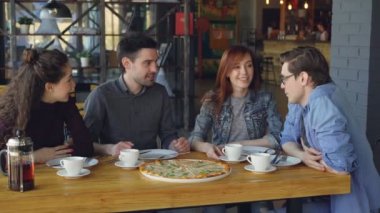 Yakın arkadaş genç erkek ve kadınların samimi kafede lezzetli yemek yeme ve konuşmaya büyük pizza paylaşıyorsunuz. Dostluk, Gastronomi ve iletişim kavramı.