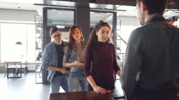 Une jeune femme bavarde avec la caissière au comptoir du café tandis que des gens impatients font la queue et attendent. Intérieur de café moderne, tables et chaises sont visibles . — Video